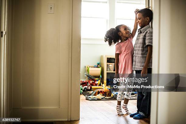 girl measuring brothers height - 兄弟姉妹 ストックフォトと画像