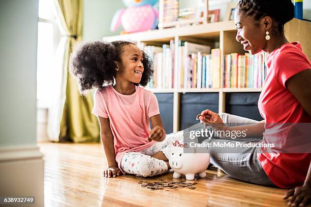 mother and daughter putting money in piggybank - happy piggy bank stock pictures, royalty-free photos & images