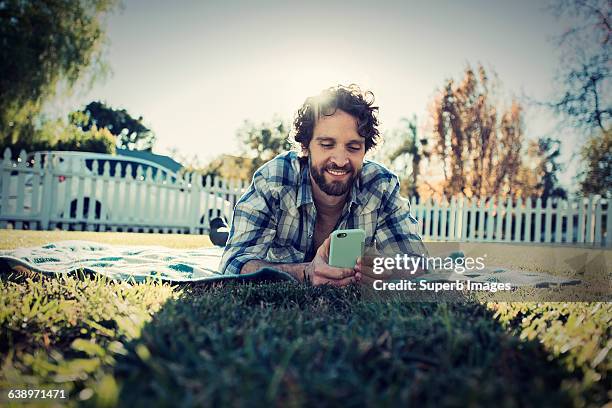 man checks cell phone in front yard - allongé sur le devant photos et images de collection