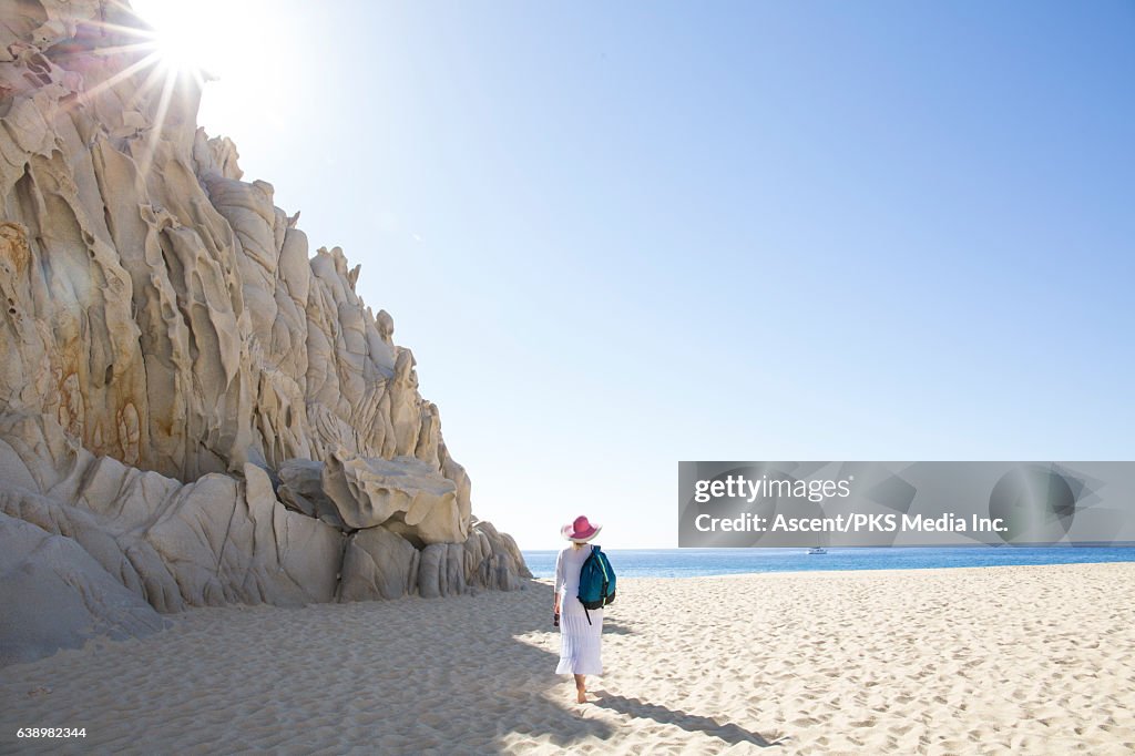 Woman walks along beach below rock cliffs