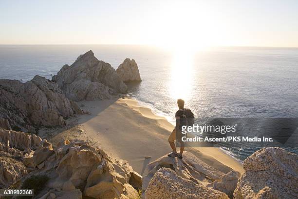 man looks out across beach and sea from rock cliffs - baja california sur fotografías e imágenes de stock