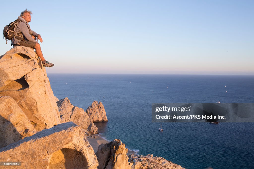 Male hiker rests on cliff edge, high above sea