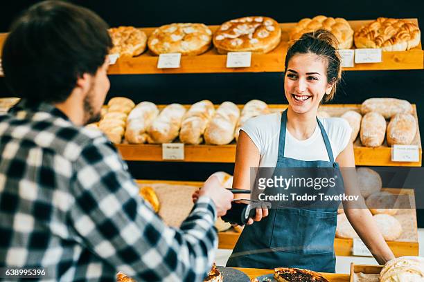 junger mann, der kontaktlos in einer bäckerei bezahlt - brot einkaufen stock-fotos und bilder
