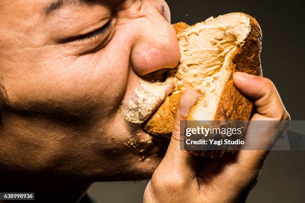 mid adult man eating peanut butter toast,close up shot - brot mund stock-fotos und bilder