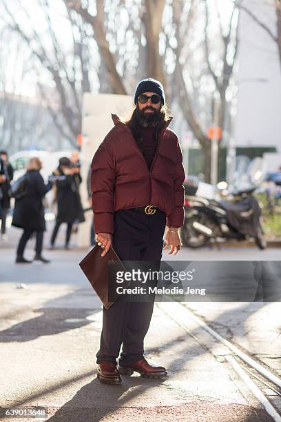 Graziano Di Cinto wears a slouchy red puffer jacket, Gucci belt, blue trousers, and a leather Hugo Boss portfolio during Milan Men's Fashion Week...