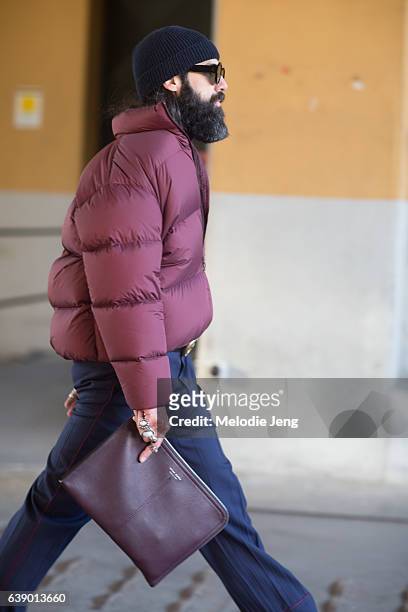 Graziano Di Cinto wears a slouchy red puffer jacket, Gucci belt, blue trousers, and a leather Hugo Boss portfolio during Milan Men's Fashion Week...