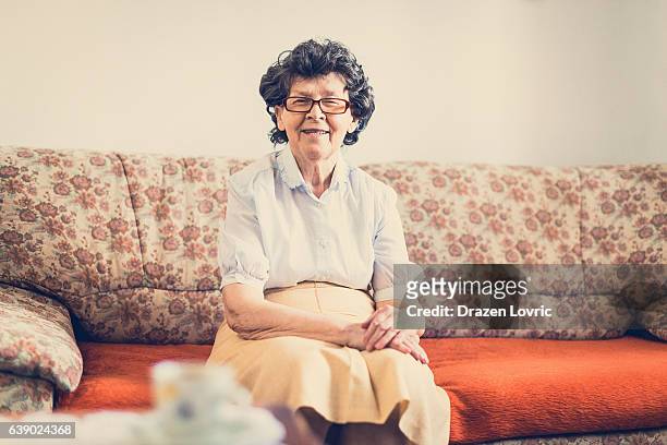aging with smile - senior woman sitting on couch - oost europese cultuur stockfoto's en -beelden