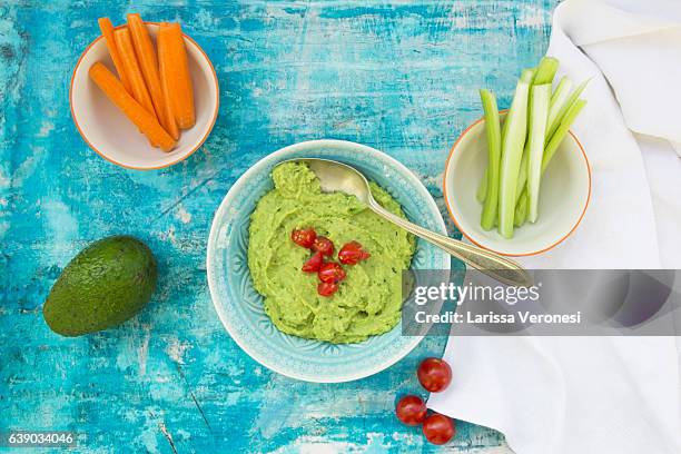 bowl of guacamole, avocado and tomatoes on blue surface - guacamole stock pictures, royalty-free photos & images