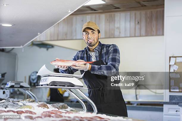 hispanic man working in seafood market, holding fish - viswinkel stockfoto's en -beelden