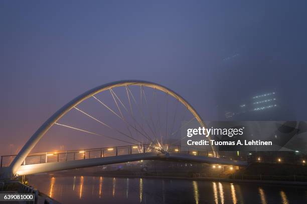 foggy view of a river, lit bridge and skyscraper in incheon, south korea in the evening. - songdo ibd stock pictures, royalty-free photos & images