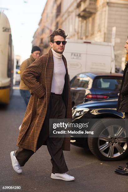 Guest wears an orange tartan plaid overcoat over a white turtleneck, brown trousers, and white sneakers during Milan Men's Fashion Week Fall/Winter...