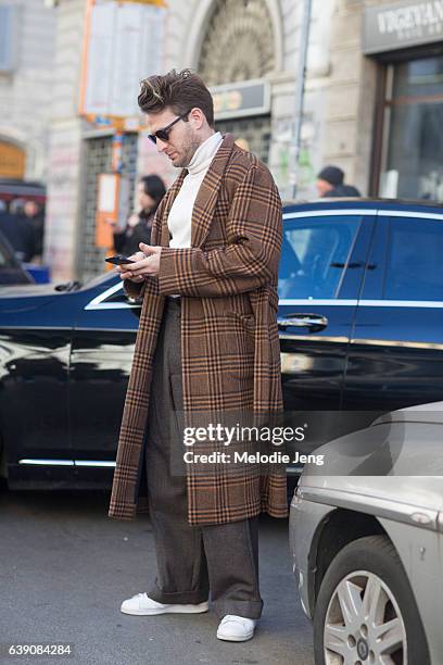 Guest wears an orange tartan plaid overcoat over a white turtleneck, brown trousers, and white sneakers during Milan Men's Fashion Week Fall/Winter...