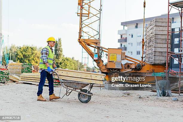 un travailleur de la consturction pousse une brouette sur un chantier de construction - brouette photos et images de collection