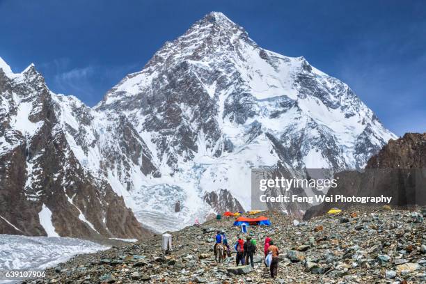 trekker & porter walking towards broad peak base camp with k2 in background, central karakoram national park, gilgit-baltistan, pakistan - k2 mountain stock-fotos und bilder