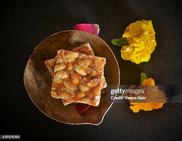 peanut brittle-peanut chikki in a metal bowl with marigold flowers-uttarayan - makar sankranti 個照片及圖片檔