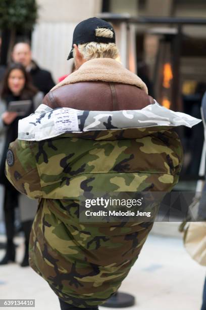 Luke Day wears a red Vetements x Canada Goose camouflage down parka over a brown shearling jacket and a black cap outside the Balenciaga show at...