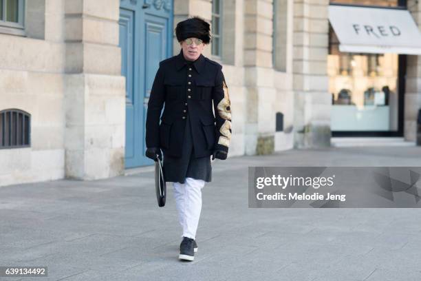 Nick Wooster wears a fur hat, military-style jacket, white pants, and black Nike sneakers outside the Lemaire show at Palais de la Femme on January...