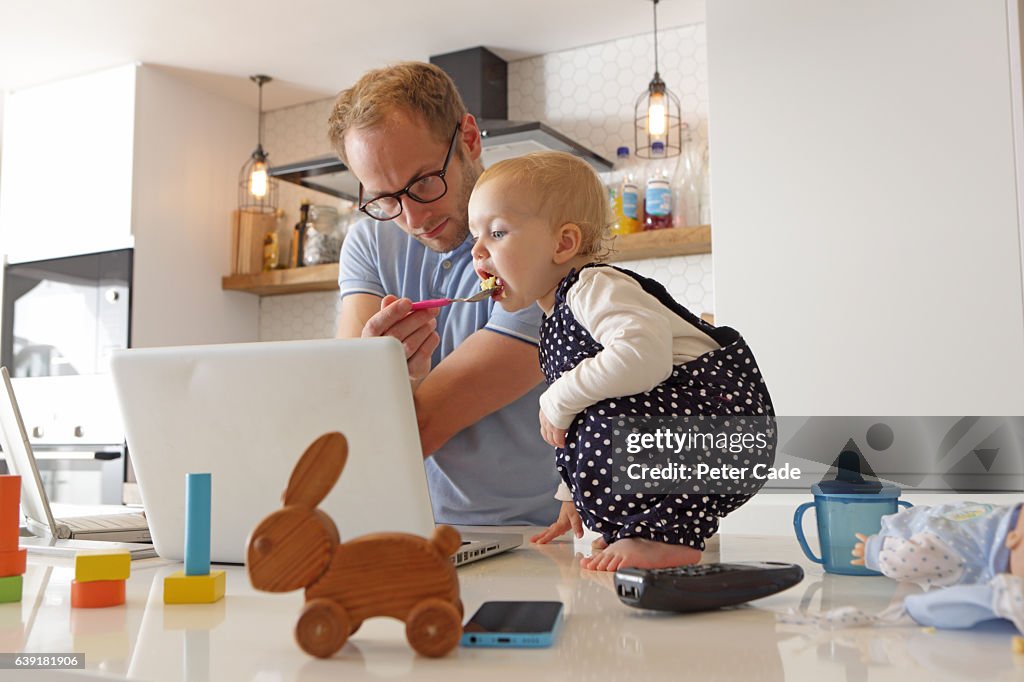 Father working on laptop whilst looking after toddler