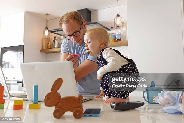 father working on laptop whilst looking after toddler - nourrir photos et images de collection