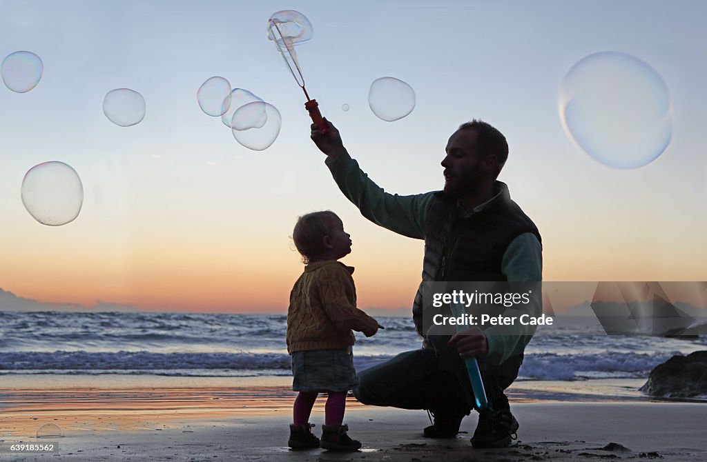 Father creating bubbles on beach with toddler