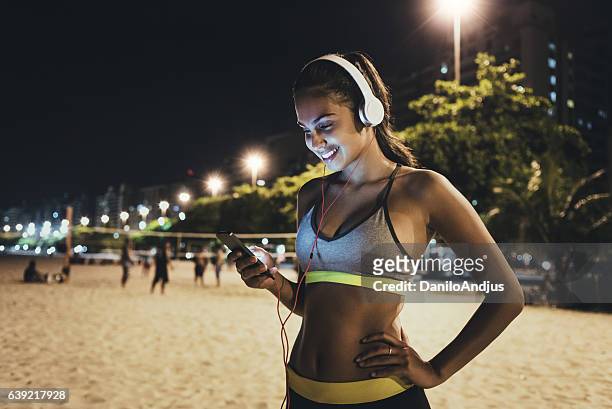jogger using her smartphone and resting - praia noite imagens e fotografias de stock