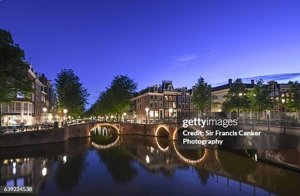 image of amsterdam at dusk with illuminated bridges reflected on canal waters, the netherlands - canal disney stock pictures, royalty-free photos & images