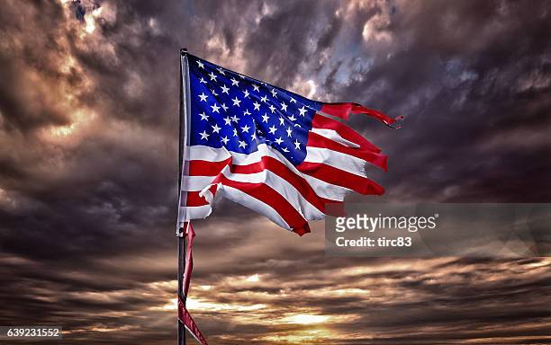 bandera estadounidense hecha jirones aleteando en un cielo ominoso - run down fotografías e imágenes de stock
