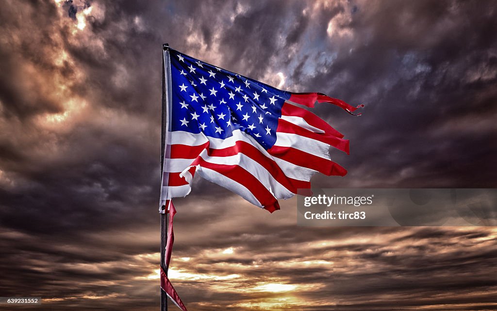 Tattered American flag flapping in ominous sky