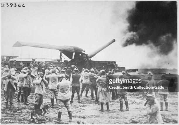 On the battlefields during World War I, a large French cannon discharges and launches a shell toward the German enemy, while several gunners stand...
