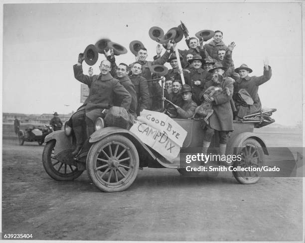 Dozen US soldiers, wearing uniforms with wool coats and raising hats toward the air, smile and wave piled up in a car on their way out of Camp Dix,...