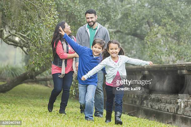 family with two playful children taking a walk in park - four people walking stock pictures, royalty-free photos & images