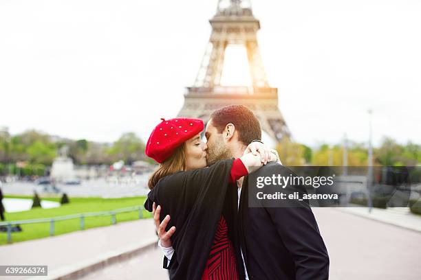 young romantic couple kissing near the eiffel tower in paris - beret cap stock pictures, royalty-free photos & images