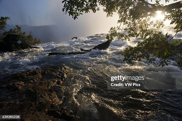 Sunset in the Victoria Falls. Victoria Falls is the result of soft sandstone that fills huge cracks in the hard basalt rock of the plateau. As the...