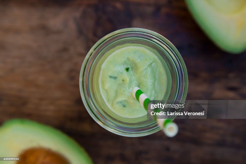 Glass of avocado smoothie and avocados on wood