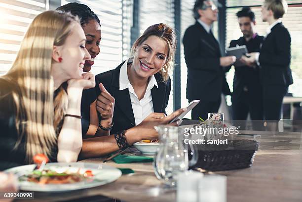 geschäftsfrauen, die beim business lunch auf ssmartphone schauen und lachen - breakfast meeting stock-fotos und bilder
