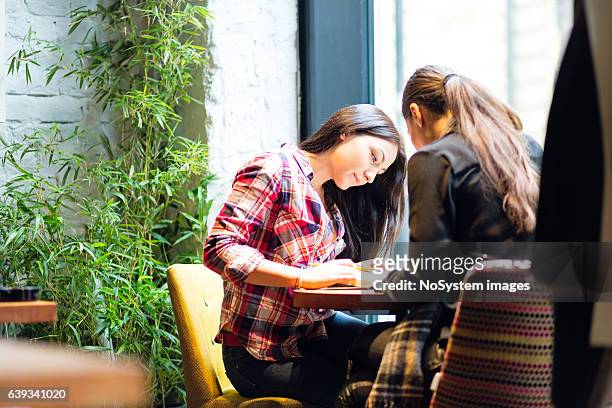 girl friends sitting together in cafe, studying - publik stockfoto's en -beelden