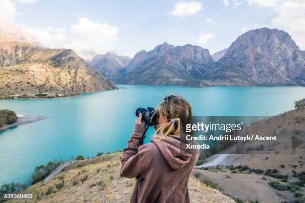 young woman takes picture across mountain lake - digitale spiegelreflexcamera stockfoto's en -beelden