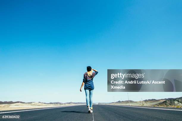 young woman walks along long rural highway - horizonte sobre tierra fotografías e imágenes de stock