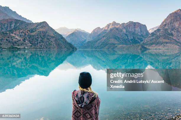 young woman looks out across mountain lake - tajikistan stock pictures, royalty-free photos & images