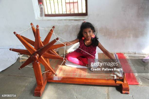 January 10. A young visitor tries her hand at spinning the yarn. The unusually sparse home of the Mahatma Gandhi, called the Father of India....