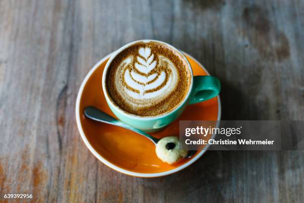 flat white coffee on an orange saucer with a biscotti on the side - christine wehrmeier stock pictures, royalty-free photos & images