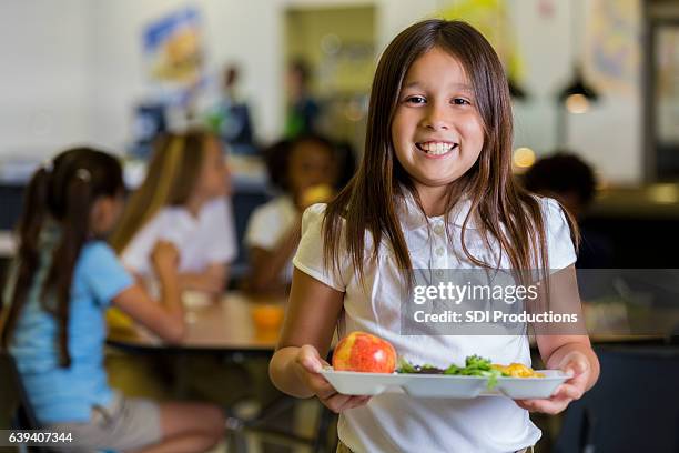 glückliche grundschulmädchen mit gesundem essen in der cafeteria - child holding apples stock-fotos und bilder