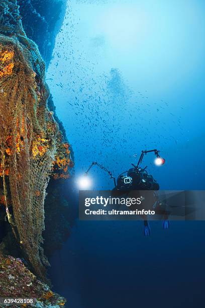 fotografo fotografare esplorare la barriera corallina e scuba diver vecchia rete da pesca - macchina fotografica subacquea foto e immagini stock