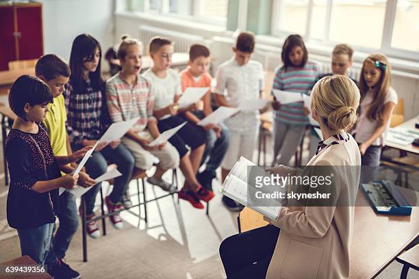 elementary school teacher singing with children in the classroom. - choir imagens e fotografias de stock