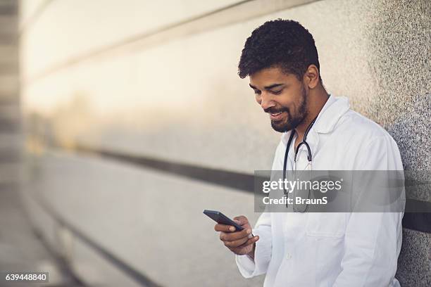 glücklicher afroamerikanischer arzt mit smartphone. - doctor using smartphone stock-fotos und bilder