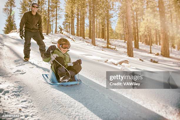 father watching son sled down a hill - mammoth lakes stock pictures, royalty-free photos & images