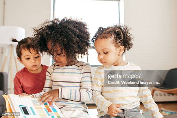 three kids in daycare with book - multilingual stockfoto's en -beelden