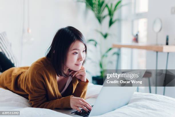 woman student using laptop in bedroom - surfing-the-net stock pictures, royalty-free photos & images