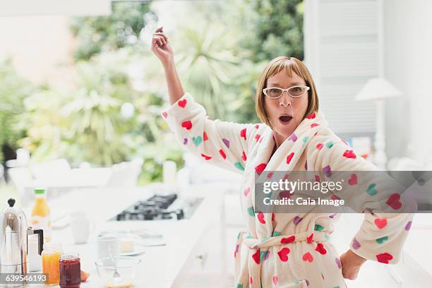 portrait of playful mature woman in bathrobe dancing in kitchen - une seule femme d'âge mûr photos et images de collection