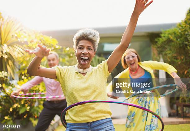 portrait playful mature adults spinning with plastic hoops in garden - jogar ao arco imagens e fotografias de stock